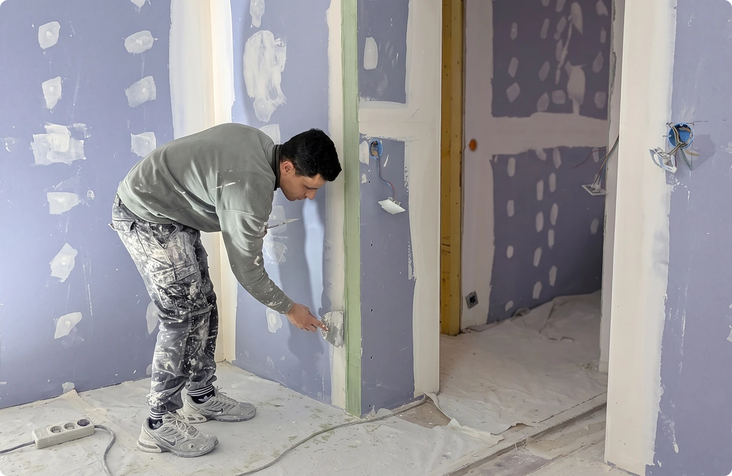 Structure de faux-plafond métallique apparente au-dessus d'une cloison en placo bleu avec porte en bois intégrée.
