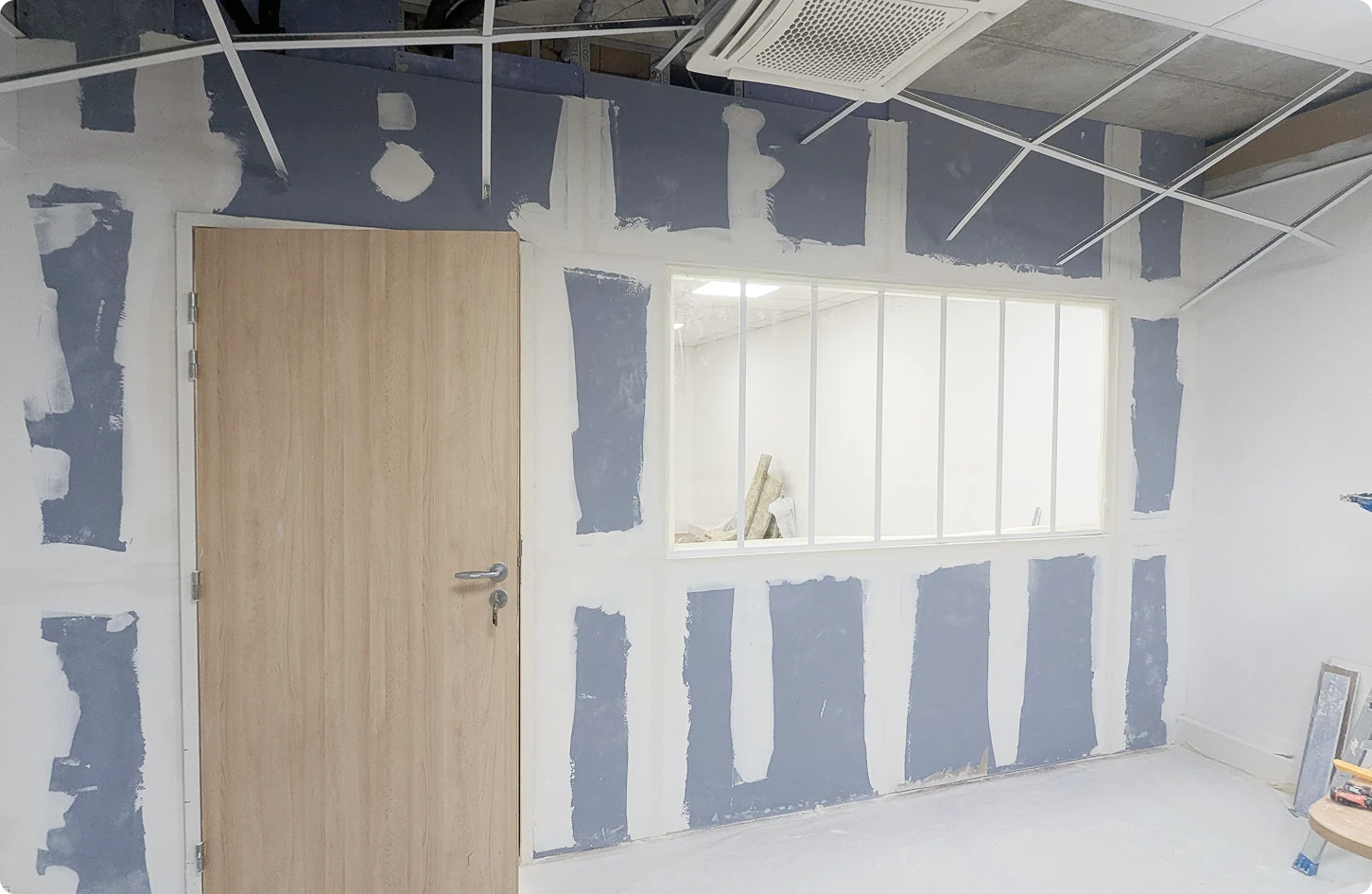 Cloison en placo bleu avec joints blancs et grand cadre de verrière au centre dans un local professionnel en rénovation.
